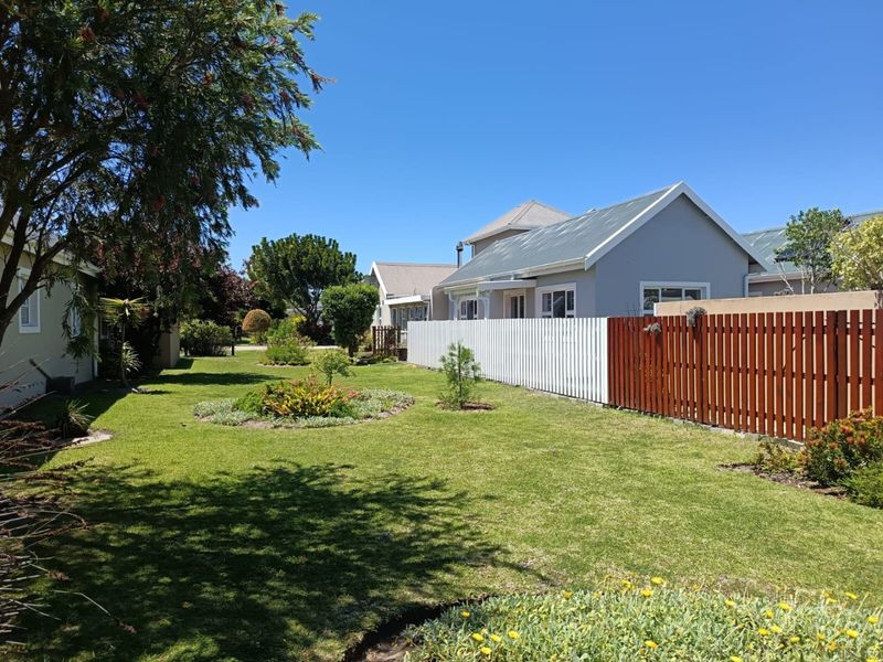 A well-maintained residential garden featuring a manicured lawn, landscaped garden beds, and a combination of white and timber fencing.
