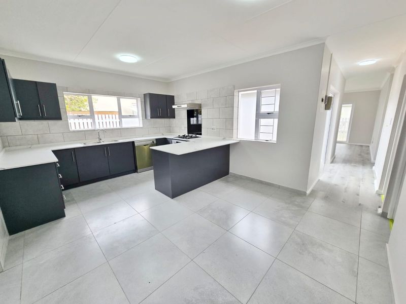 Modern kitchen featuring dark cabinetry, stone countertops, integrated gas hob, extractor fan, and neutral tiled flooring in an open-plan layout.