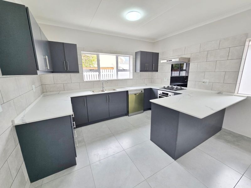 Modern kitchen featuring dark cabinetry, white quartz countertops, tiled splashback, and integrated appliances including a gas hob and oven.