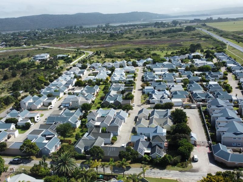 An aerial view of a residential housing estate featuring uniform pitched roof homes, paved internal roads, and surrounding natural landscape.