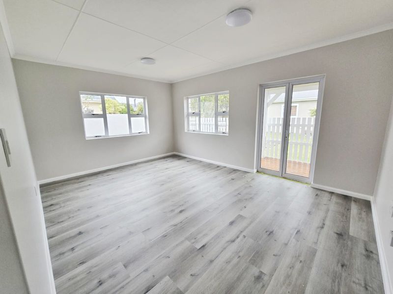 A bright, empty living room featuring modern laminate flooring, neutral walls, and glass french doors providing access to the outdoor area.