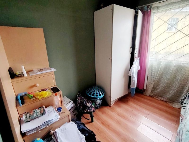 A bedroom featuring laminate flooring, a built-in wardrobe, and security bars on the window, requiring cosmetic updates to improve its overall appeal.
