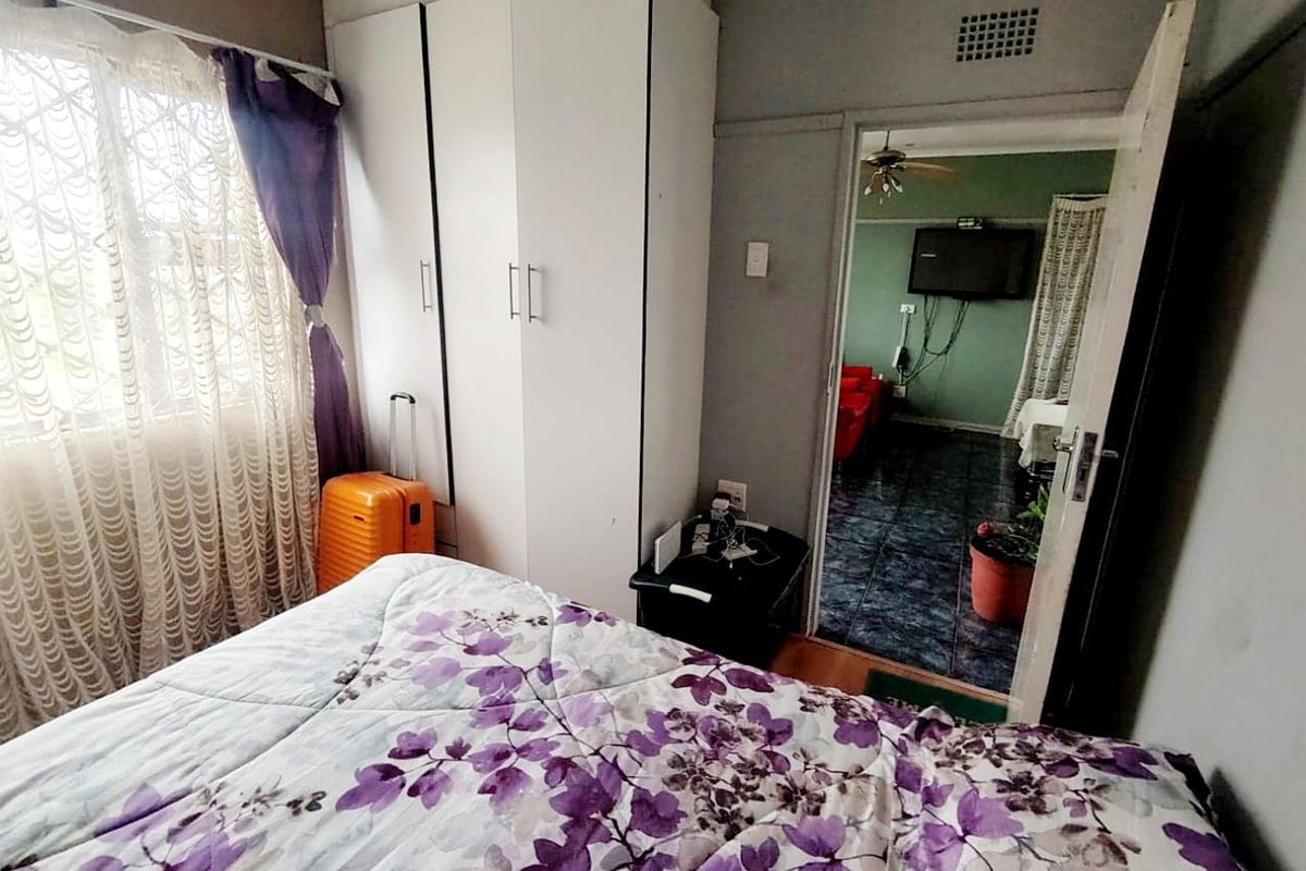 A bedroom featuring a built-in wardrobe and a view through the doorway into an adjacent living area with tiled flooring.