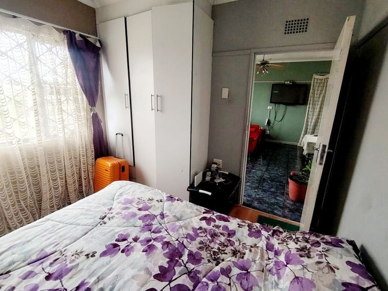 A bedroom featuring a built-in wardrobe and a view through the doorway into an adjacent living area with tiled flooring.