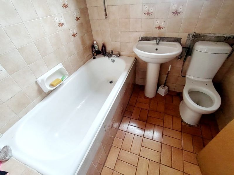 A dated bathroom featuring a standard bathtub, pedestal basin, and toilet with original ceramic wall and floor tiling in need of modernization.