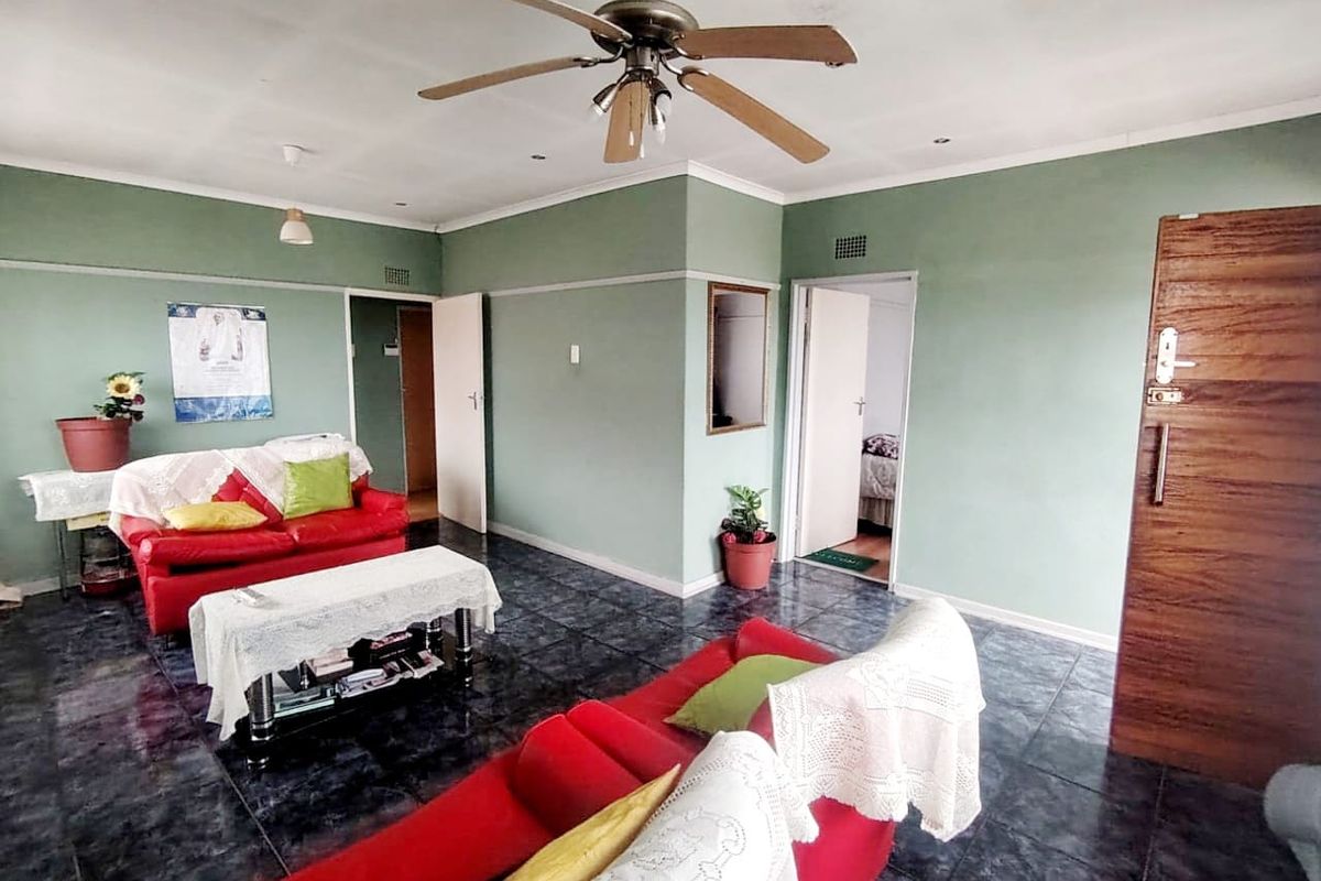 A spacious living room featuring dark tiled flooring, a ceiling fan, and neutral green walls, providing a functional and well-lit living area.
