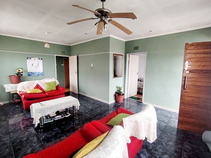 A spacious living room featuring dark tiled flooring, a ceiling fan, and neutral green walls, providing a functional and well-lit living area.