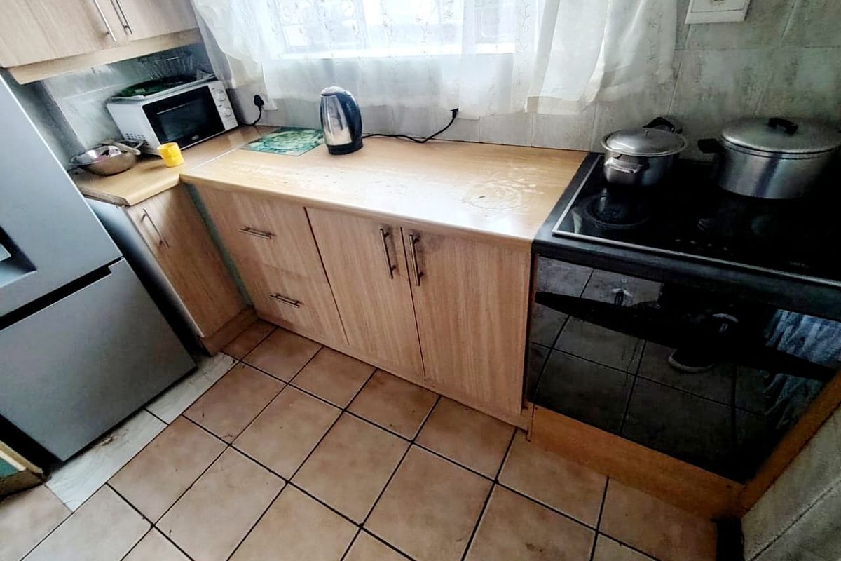 A compact kitchen featuring laminate cabinetry, tiled flooring, and a built-in electric stove, offering a functional layout in need of cosmetic updates.