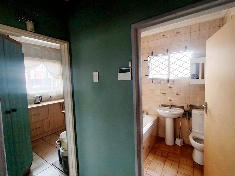 A view from a hallway looking into a bathroom and kitchen area, featuring dated finishes and standard bathroom fixtures.