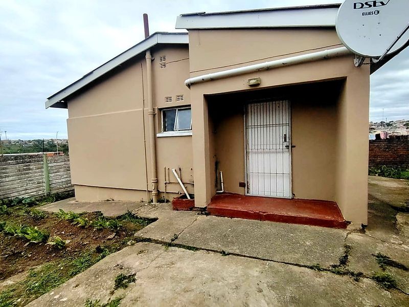 Rear exterior view of the house featuring a concrete patio area, security gate, and perimeter precast walling.