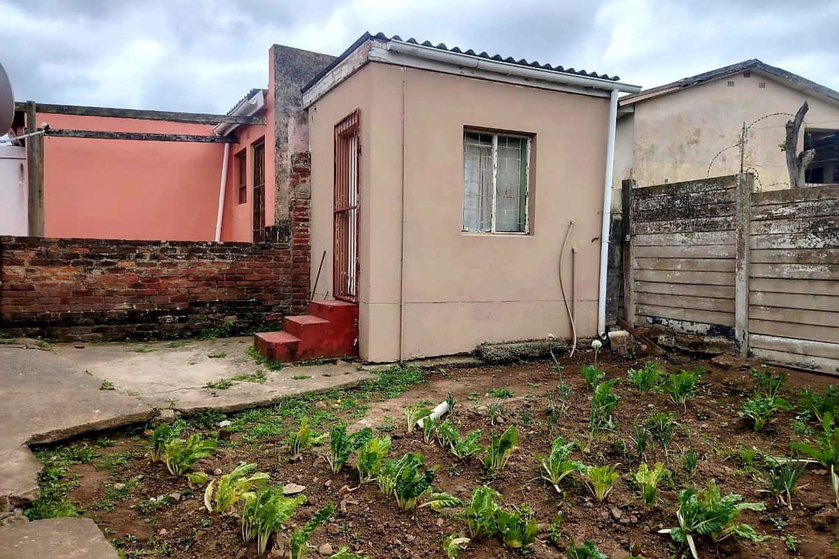 Rear exterior view of the property featuring a small concrete patio, garden area, and boundary walls.