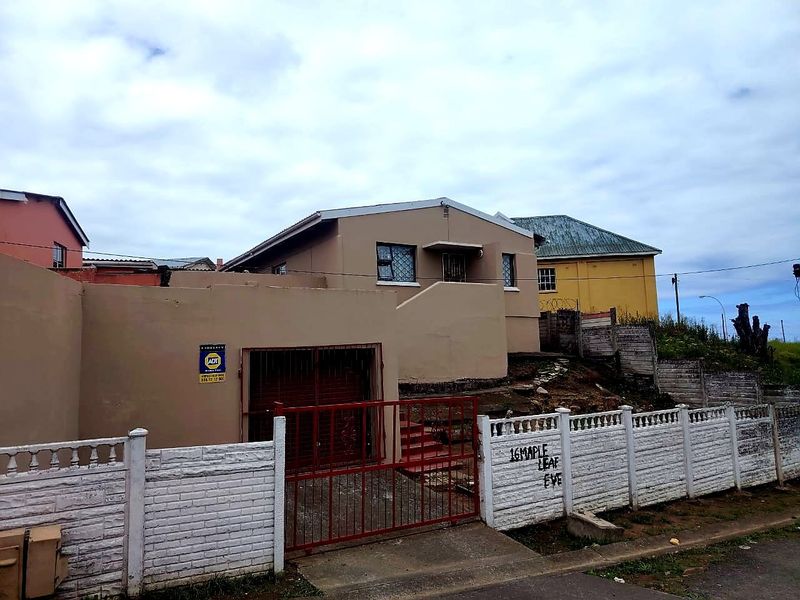 Front exterior view of a single-story house featuring a concrete boundary wall, metal driveway gate, and security alarm system.
