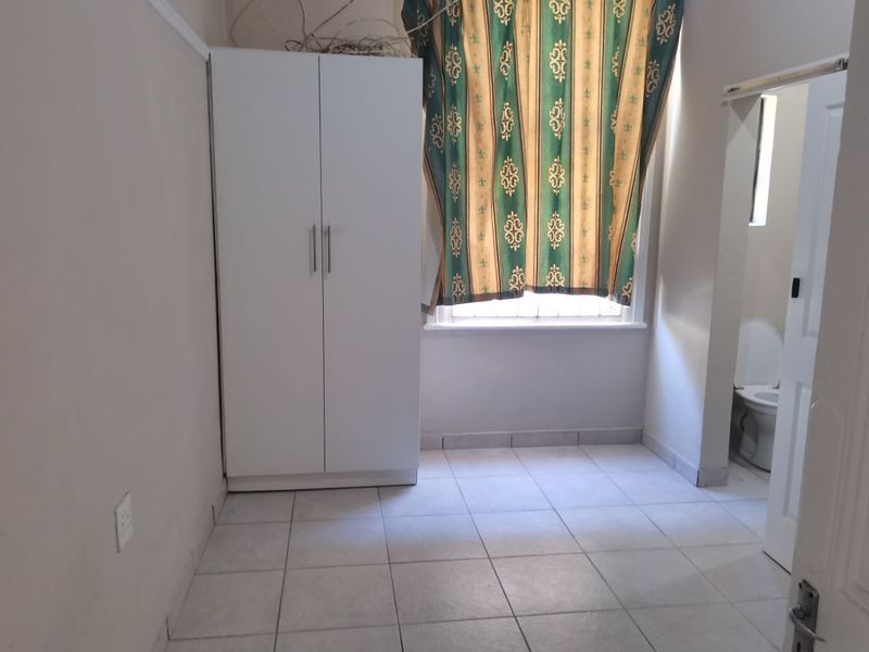 A simple bedroom featuring tiled flooring, a built-in wardrobe, and a window with security bars, offering a functional and clean living space.