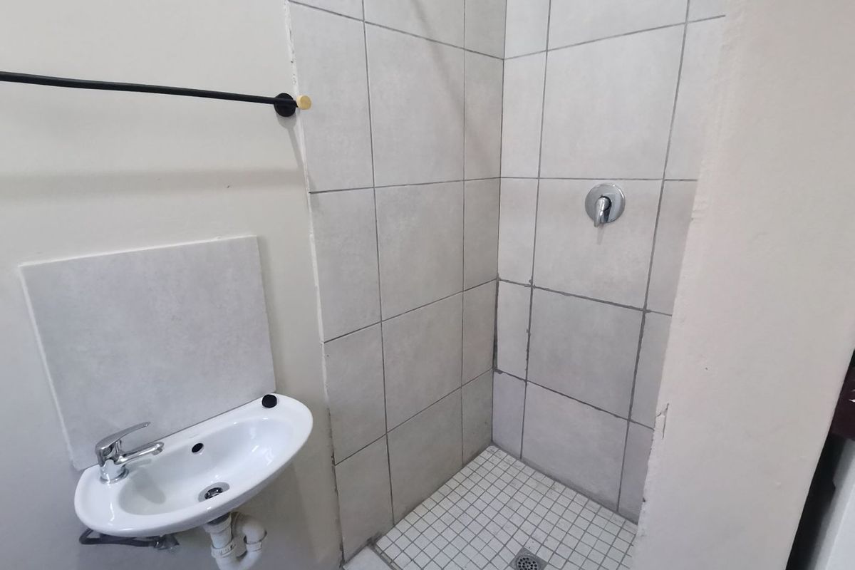 A compact bathroom featuring a wall-mounted basin and a tiled shower enclosure with basic fixtures.