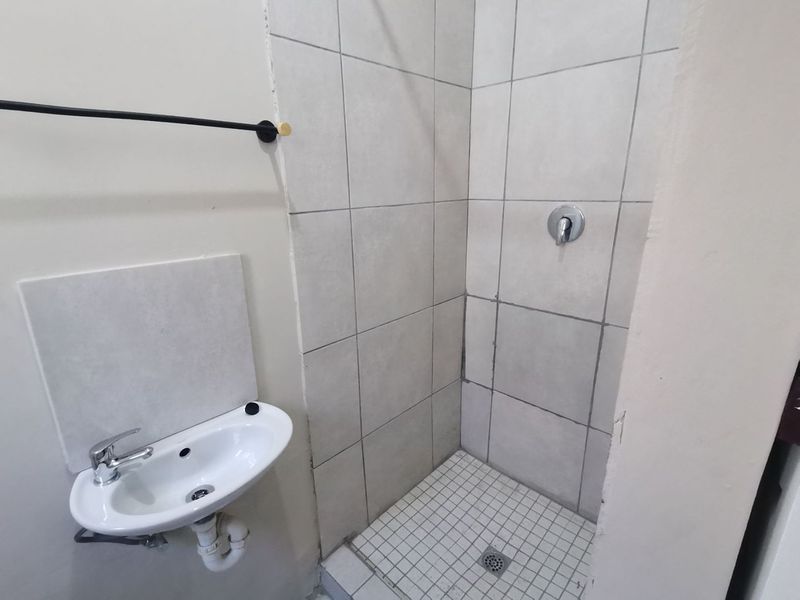 A compact bathroom featuring a wall-mounted basin and a tiled shower enclosure with basic fixtures.