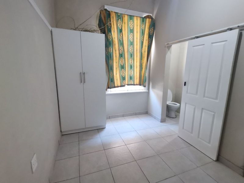 A bedroom featuring tiled flooring, a built-in wardrobe, and an adjoining en-suite toilet area with a sliding door.