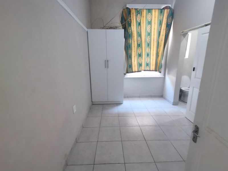 A bedroom featuring tiled flooring and a built-in wardrobe, with an adjacent bathroom visible through the doorway.