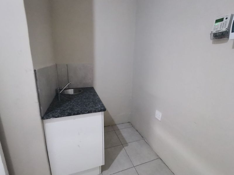 A functional laundry area featuring a built-in sink, laminate countertop, base cabinetry, and tiled flooring, providing a practical utility space.