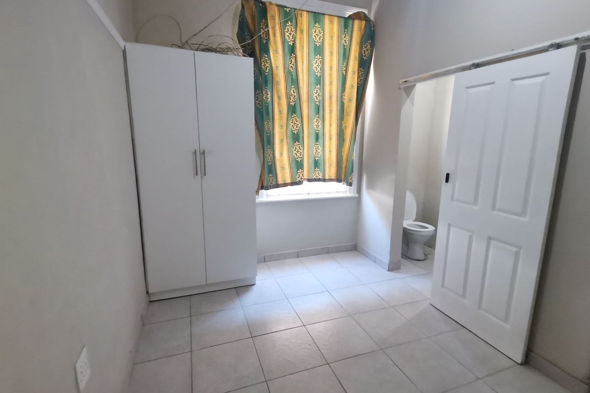 A simple bedroom featuring tiled flooring, a built-in wardrobe, and an attached en-suite toilet area.