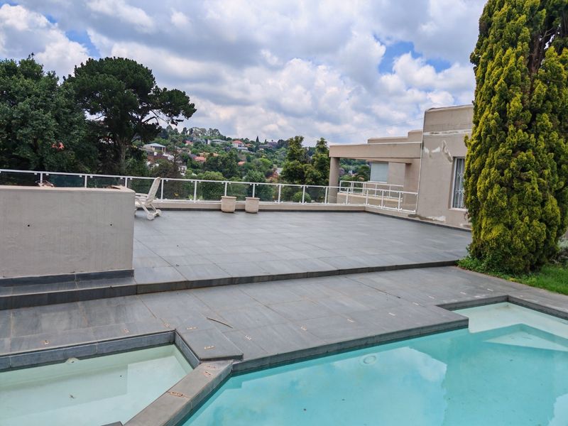 Spacious outdoor pool area featuring a large tiled deck, glass balustrades, and elevated views of the surrounding neighborhood.