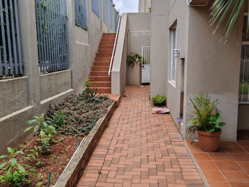 A side walkway featuring brick paving, a staircase leading to an upper level, and a retaining wall with established garden beds.