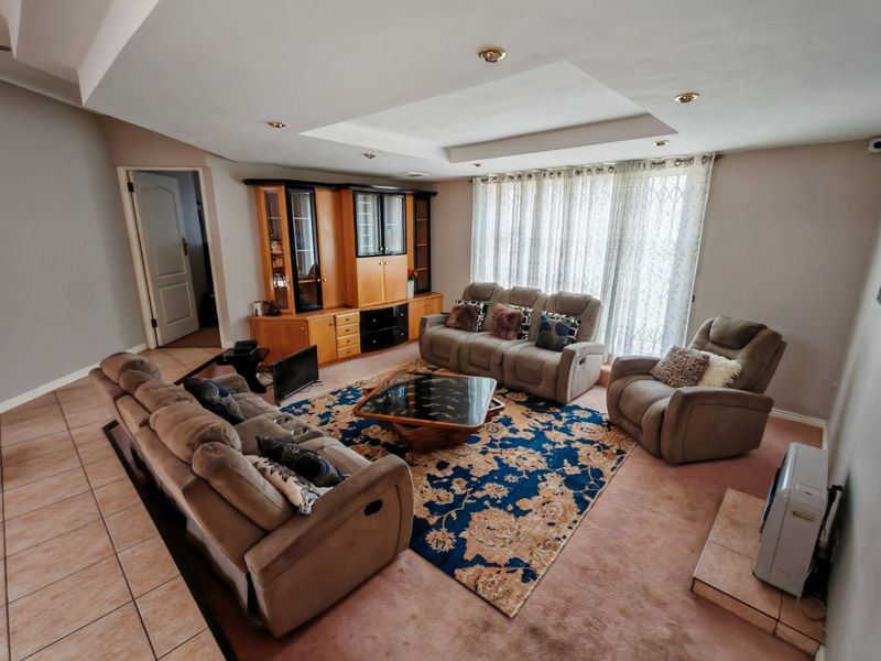 Spacious living room featuring a recessed ceiling with downlights, built-in cabinetry, and a combination of tiled and carpeted flooring with access to the outdoors.