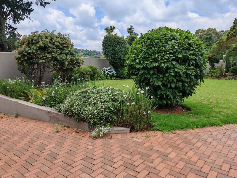 A well-maintained garden featuring a brick-paved patio area, a neat lawn, and established shrubbery with a retaining wall.