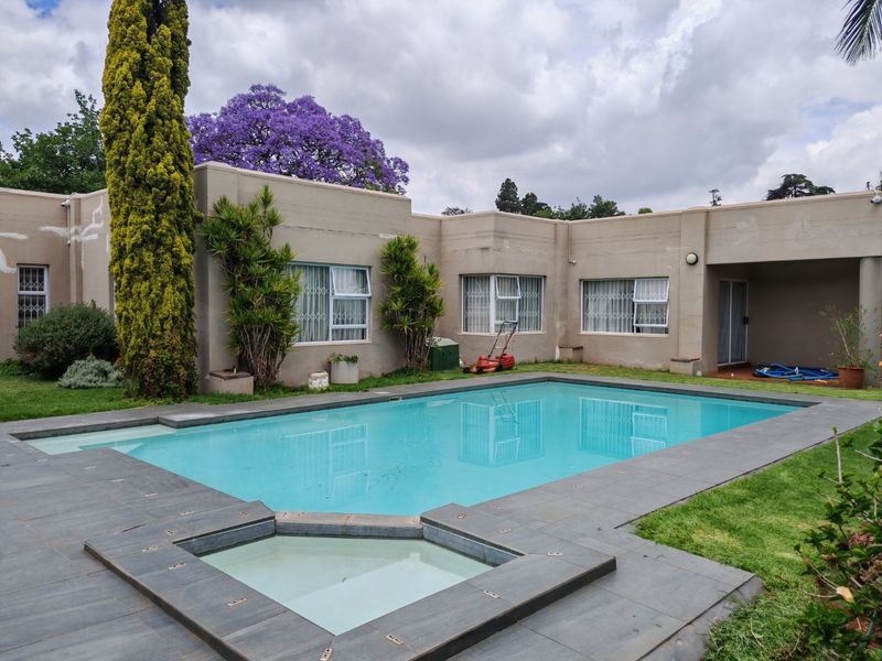 A spacious outdoor pool area featuring a tiled surround, established garden, and direct access to the rear of the house with security-fitted windows.