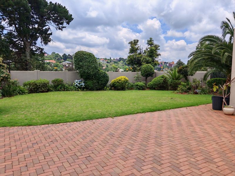 A well-maintained rear garden featuring a paved patio area, manicured lawn, and established boundary wall with mature landscaping.