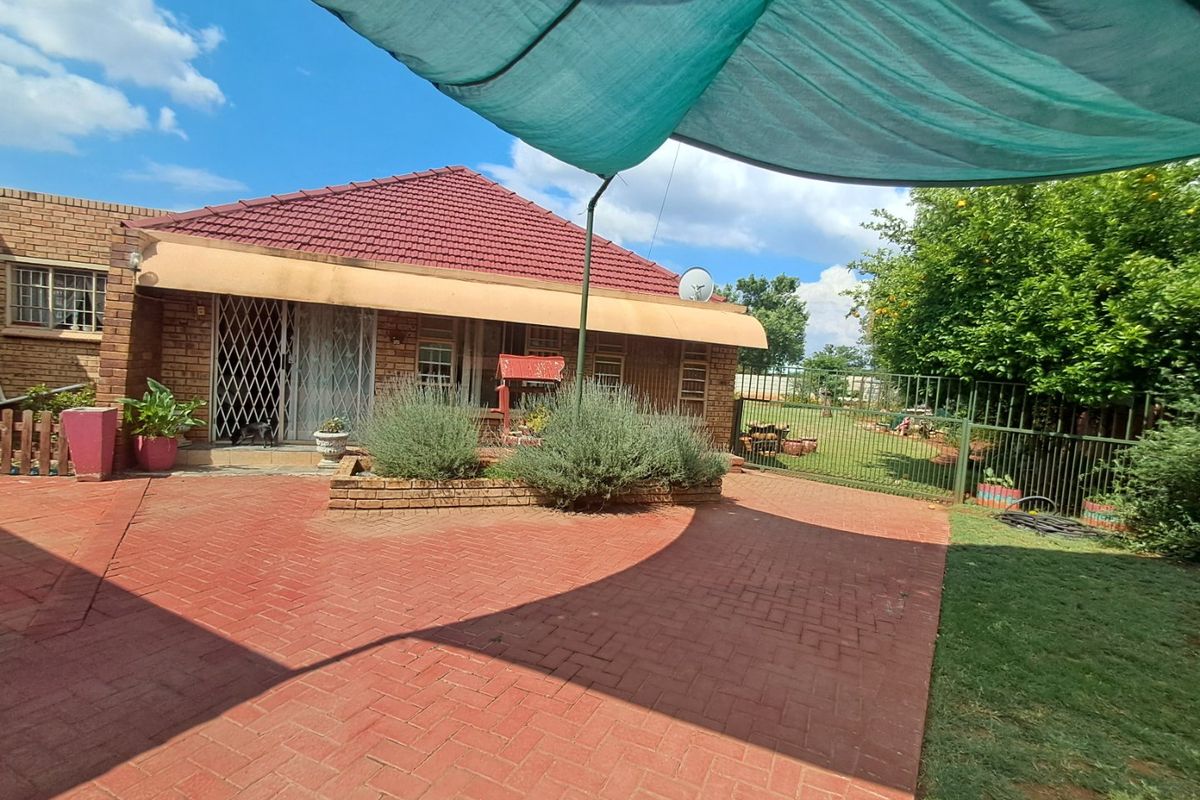 Rear exterior view of the house featuring brick paving, a tiled roof, and a shaded patio area with security gates.