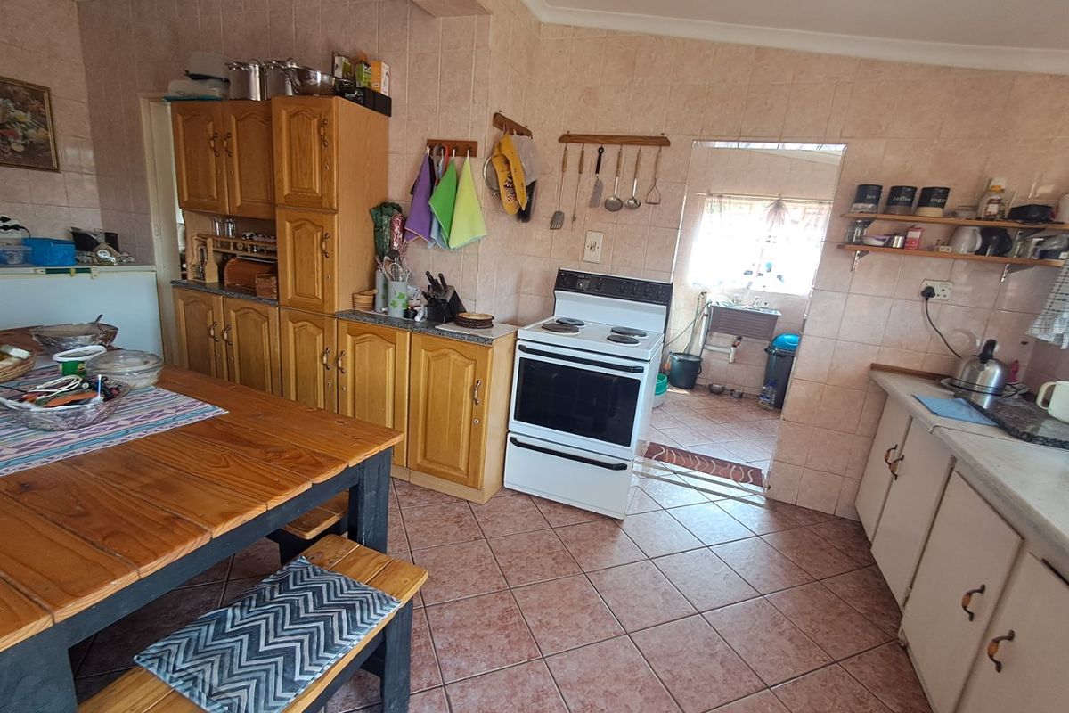 A functional kitchen featuring wooden cabinetry, tiled splashbacks, and a freestanding stove, with an adjacent scullery area visible through the doorway.