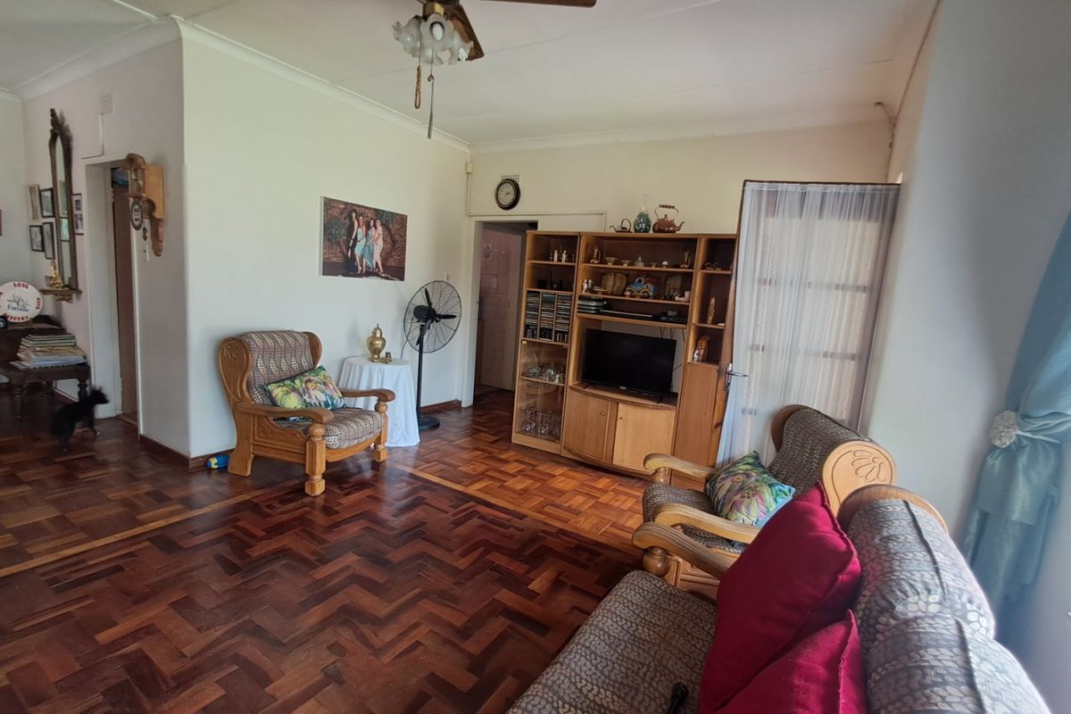 A living room featuring classic parquet flooring, a ceiling fan, and neutral wall finishes, offering a traditional foundation for modern interior updates.