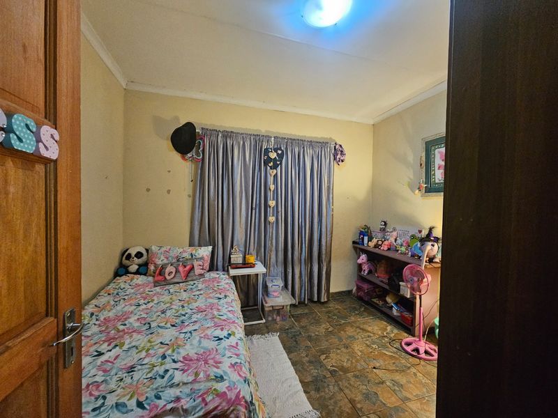 A bedroom featuring tiled flooring and neutral wall finishes, currently utilized as a child's room with standard window treatments.