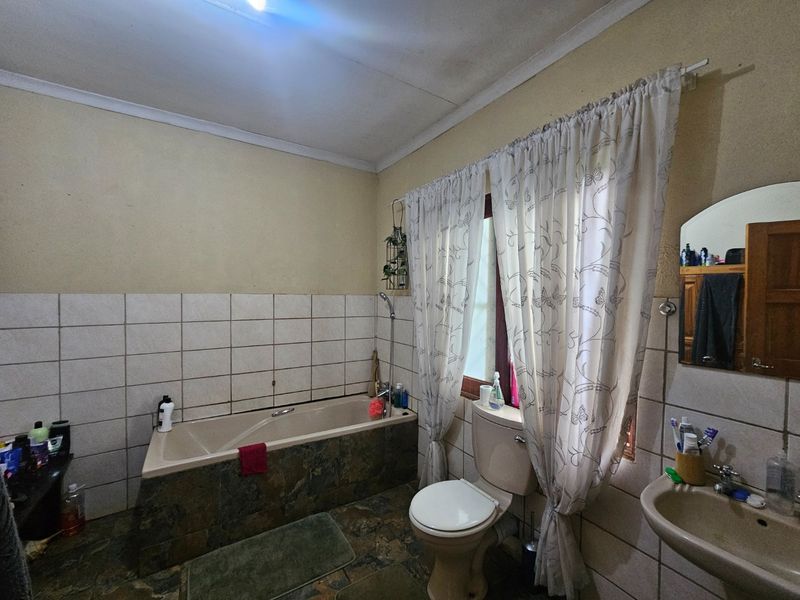 A functional bathroom featuring a built-in bathtub, pedestal washbasin, and toilet, with tiled splashbacks and neutral wall finishes.