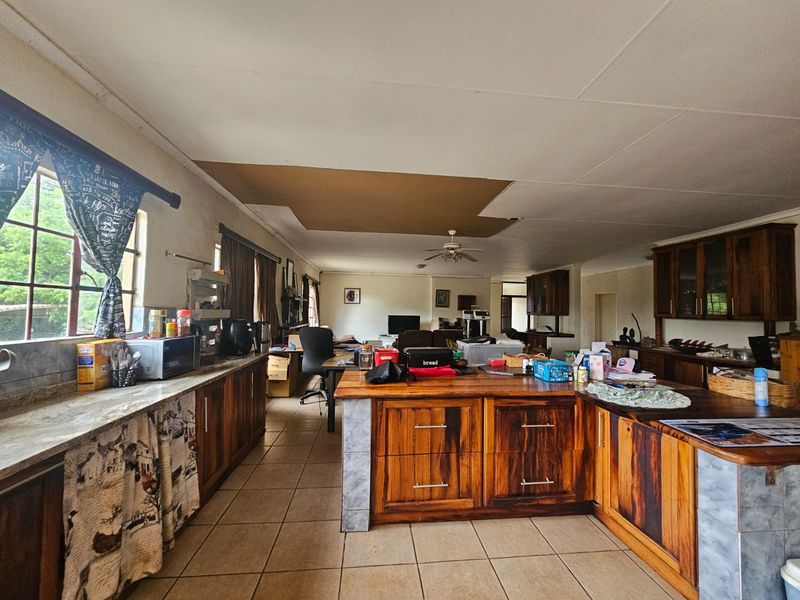 Spacious open-plan kitchen and living area featuring wooden cabinetry, tiled floors, and a ceiling fan, currently requiring ceiling repairs.