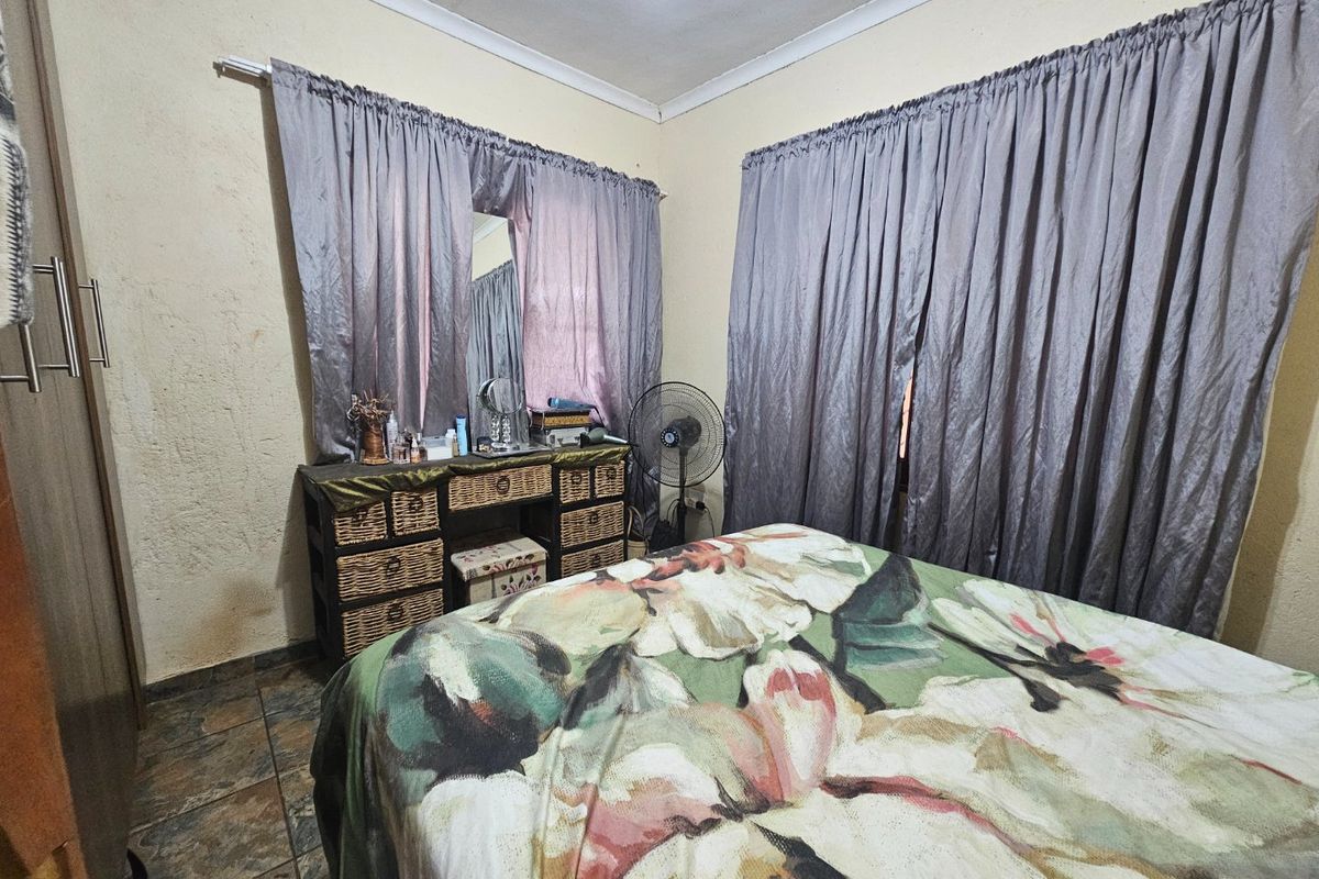 A bedroom featuring tiled flooring, coved ceilings, and a built-in wardrobe, showing signs of wear on the wall surfaces.