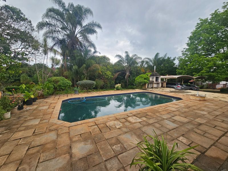 Outdoor pool area featuring stone paving, a built-in braai, and surrounding garden space, providing a functional area for outdoor entertainment.