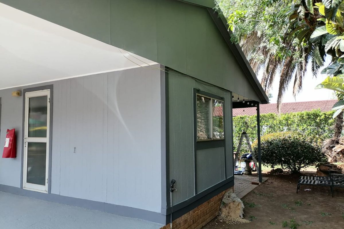 Rear exterior view of the house featuring a covered patio area, brick foundation, and painted timber-look siding.