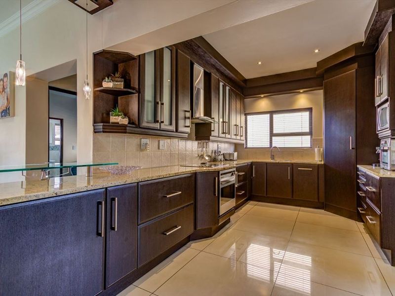 Modern kitchen featuring dark wood cabinetry, granite countertops, built-in appliances, and a breakfast bar, finished with polished floor tiles and recessed lighting.