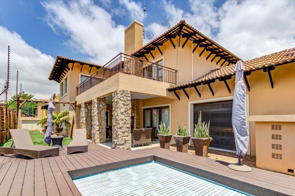 Rear exterior view featuring a swimming pool with timber decking, stone-clad pillars, and an upper-level balcony with metal railings.