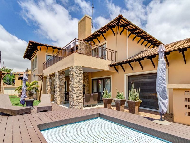 Rear exterior view featuring a swimming pool with timber decking, stone-clad pillars, and an upper-level balcony with metal railings.