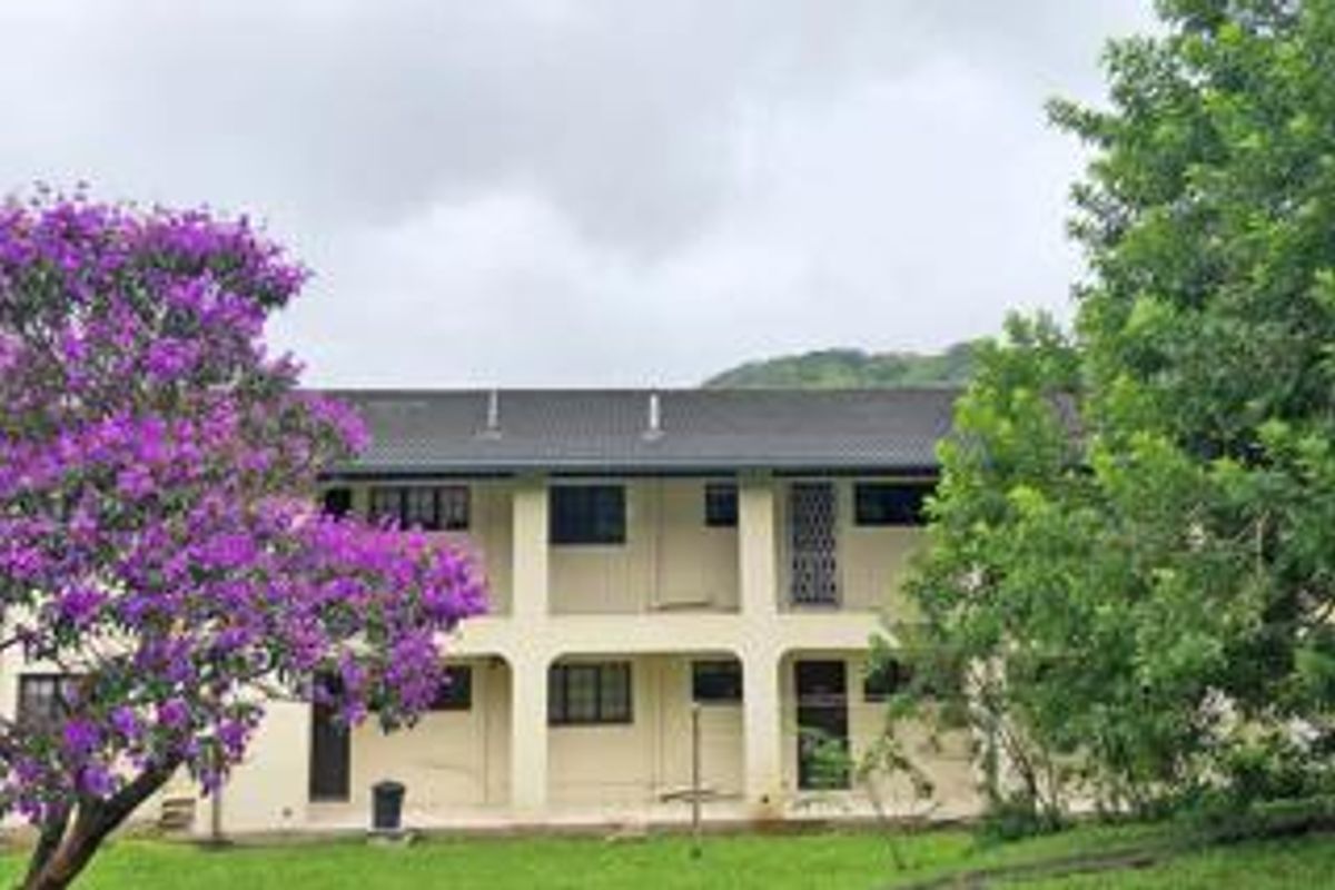 A view of the rear exterior facade of the apartment building, featuring a two-story structure with covered walkways and established garden surroundings.