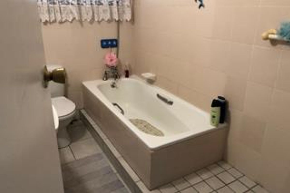A functional bathroom featuring a built-in bathtub, standard toilet, and tiled wall finishes, offering a dated aesthetic ready for modernization.