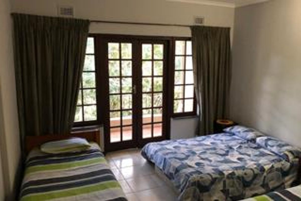 A bedroom featuring tiled flooring and double glass-paned doors that open onto a balcony, providing natural light and outdoor access.
