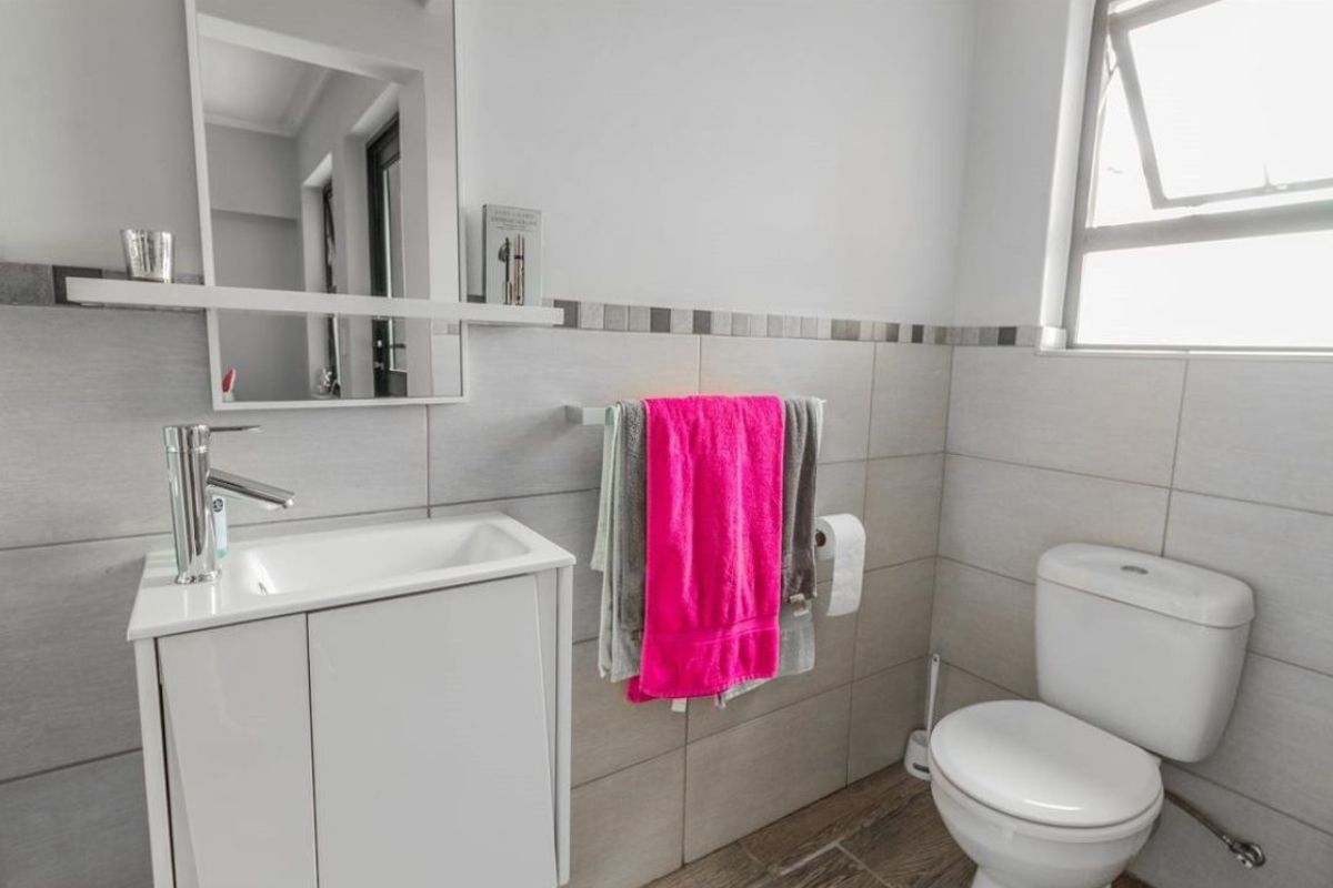 A modern bathroom featuring a vanity cabinet with basin, wall-mounted mirror, toilet, and neutral wall and floor tiling.
