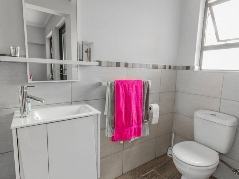 A modern bathroom featuring a vanity cabinet with basin, wall-mounted mirror, toilet, and neutral wall and floor tiling.