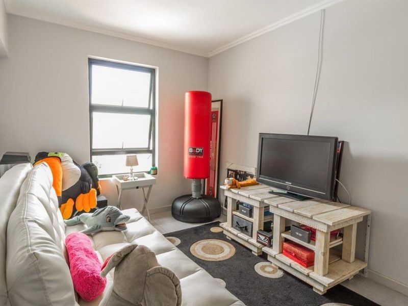A functional living room featuring tiled flooring, coved ceilings, and an aluminium window frame, providing a neutral base for potential interior updates.