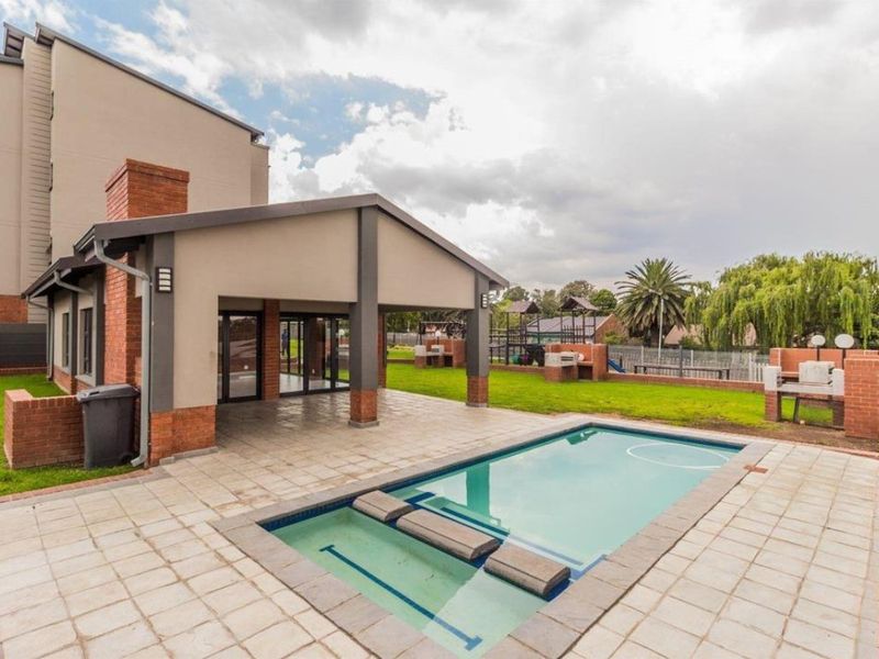 Communal outdoor area featuring a swimming pool, covered patio with built-in braai facilities, and landscaped garden space.