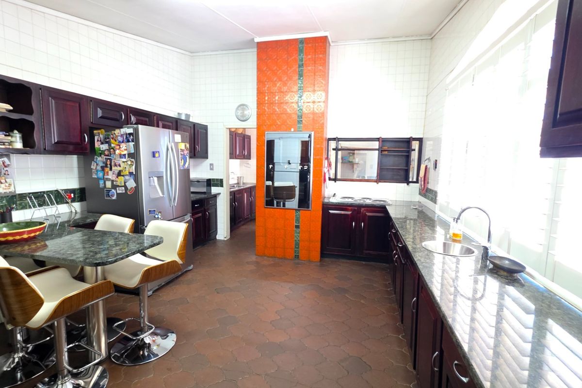 Spacious kitchen featuring dark wood cabinetry, granite countertops, a central tiled feature wall, and integrated oven, offering a functional layout with ample workspace.