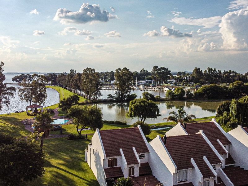 Aerial view of a residential estate featuring white townhouses with tiled roofs, expansive green lawns, a swimming pool, and scenic waterfront views.